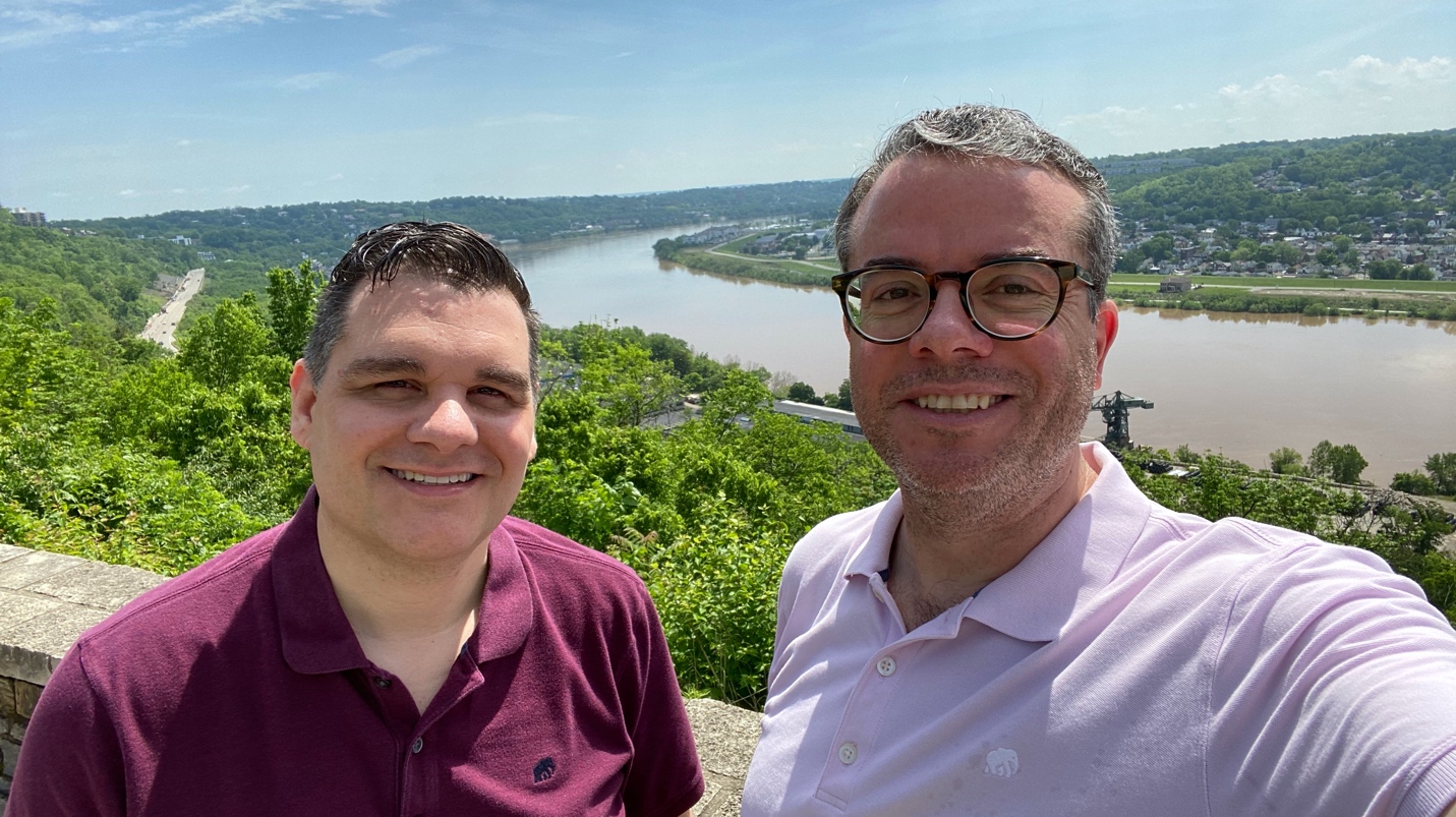 A smiling person standing in front of a mountain
Description automatically generated